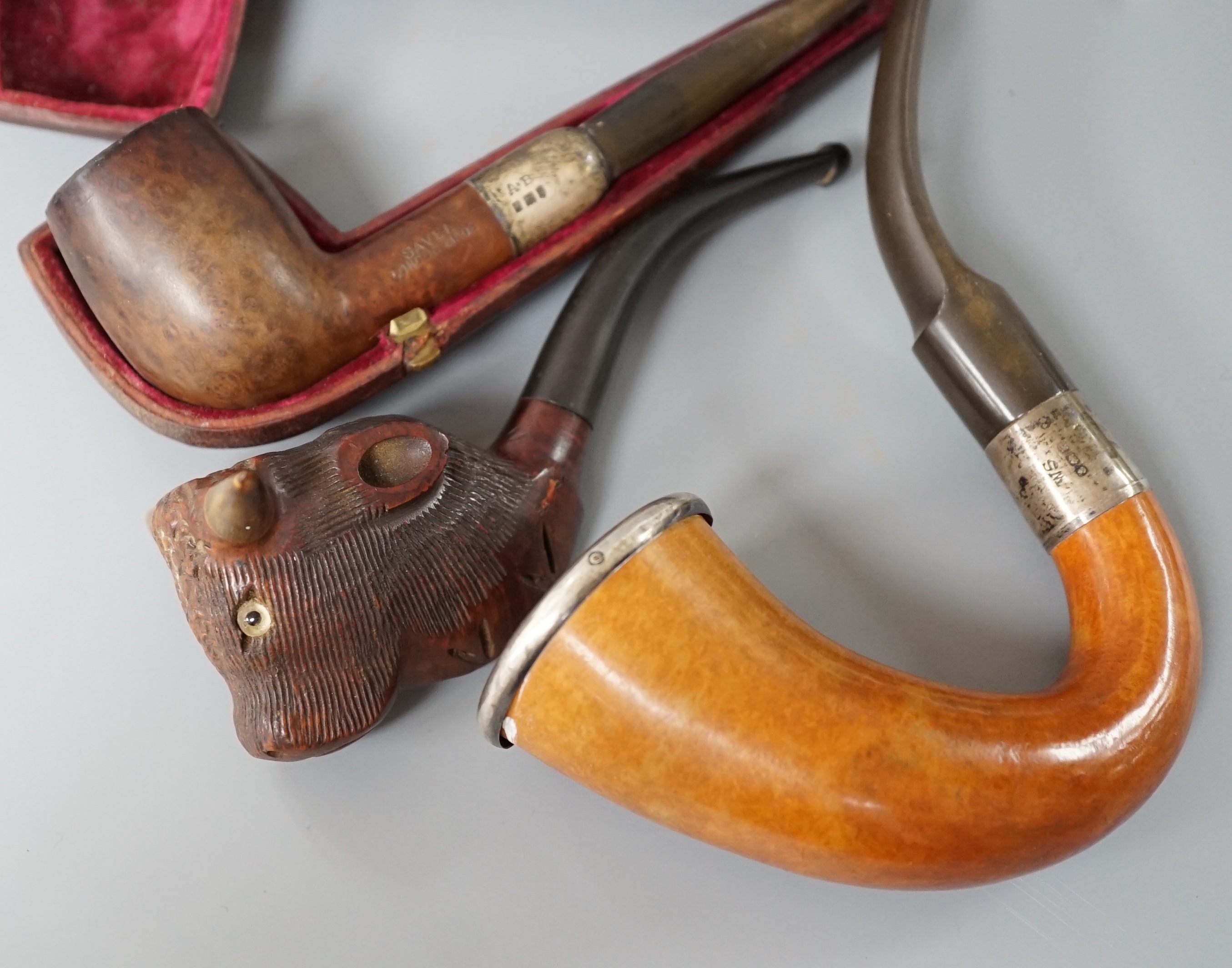 A cased Savel burr wood smokers pipe with silver collar, another pipe with silver collar and rim together with a novelty carved wood and horn ‘cow’ pipe